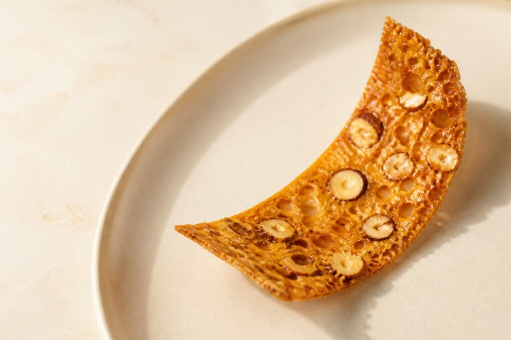 Slender caramel arc shapes the honey-hazelnut tuile