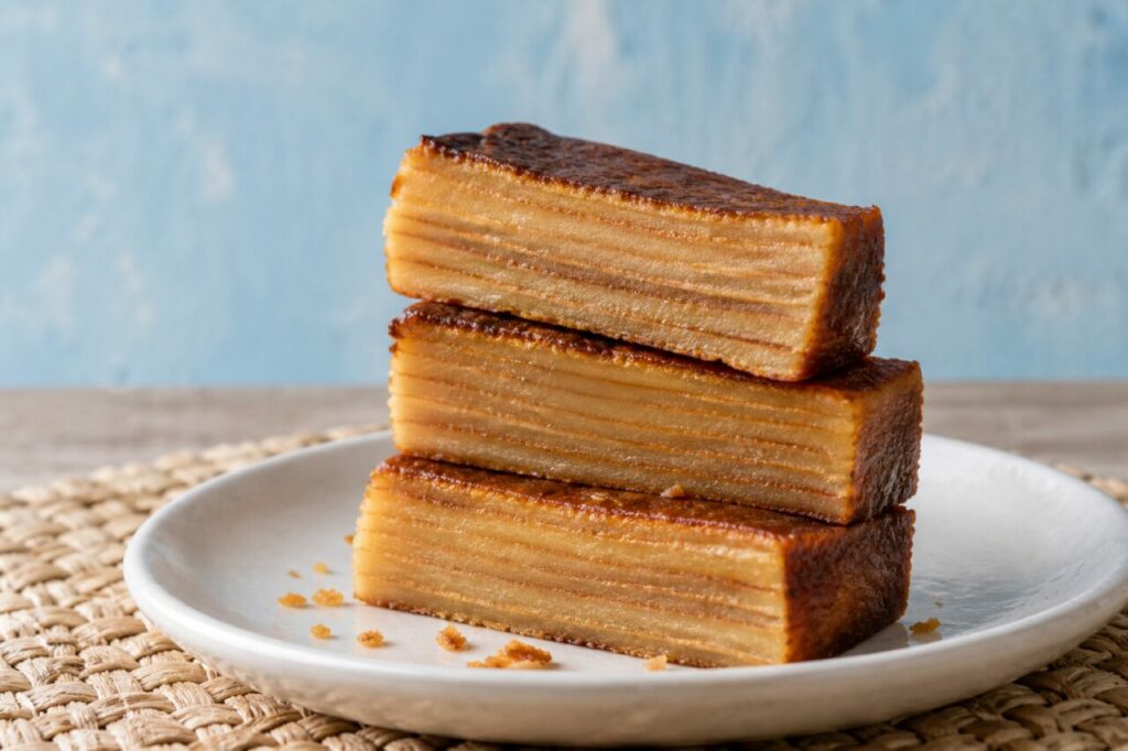 Stacked bebinca pieces on a white plate against pale blue