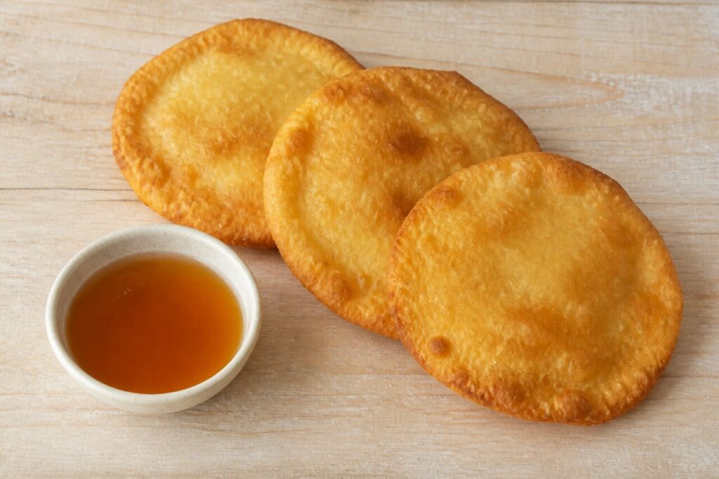 Douceur chilienne traditionnelle — sopaipillas rondes frites, dorées, accompagnées d’un petit bol de sirop ambré