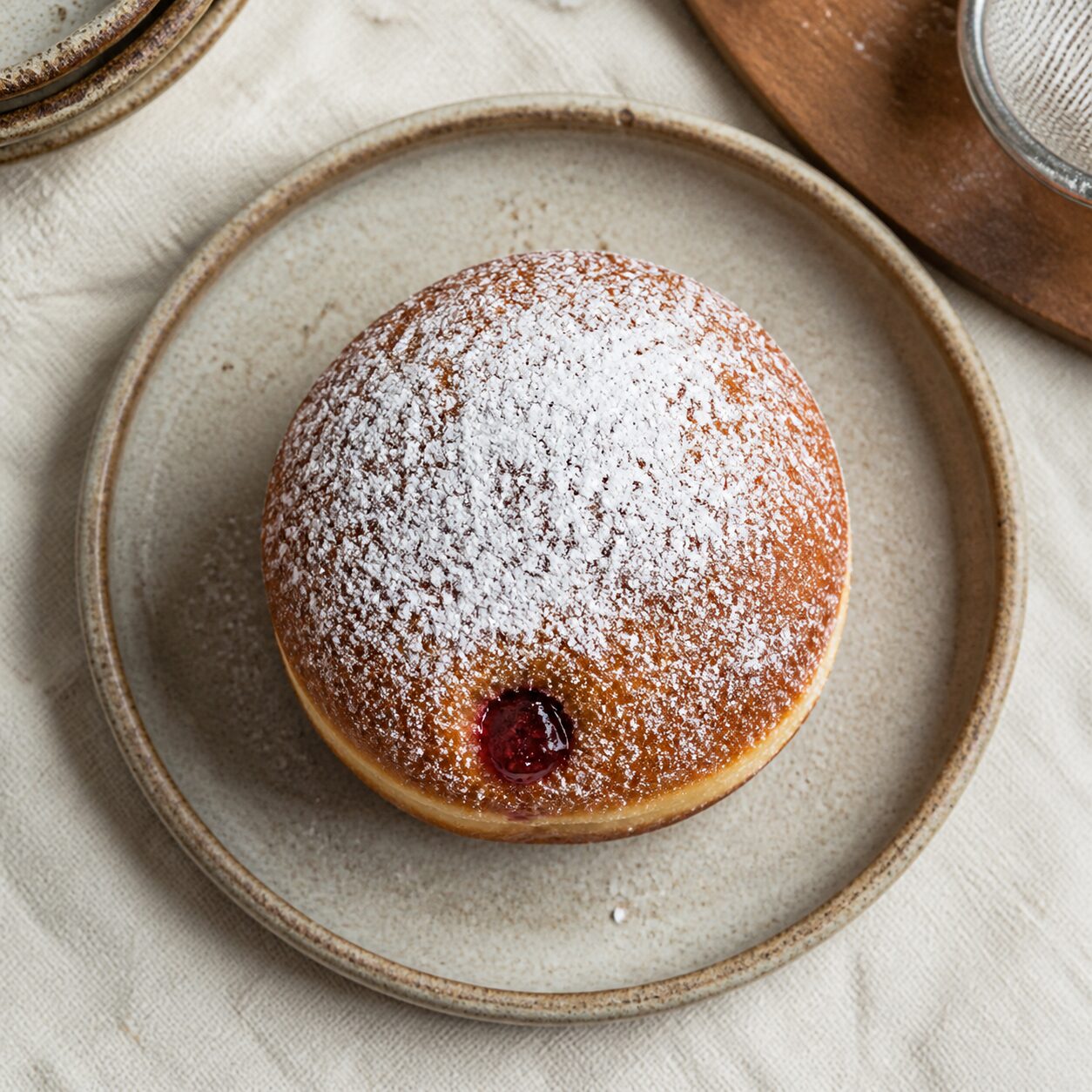 The Polish pączek wears icing sugar over its golden dome