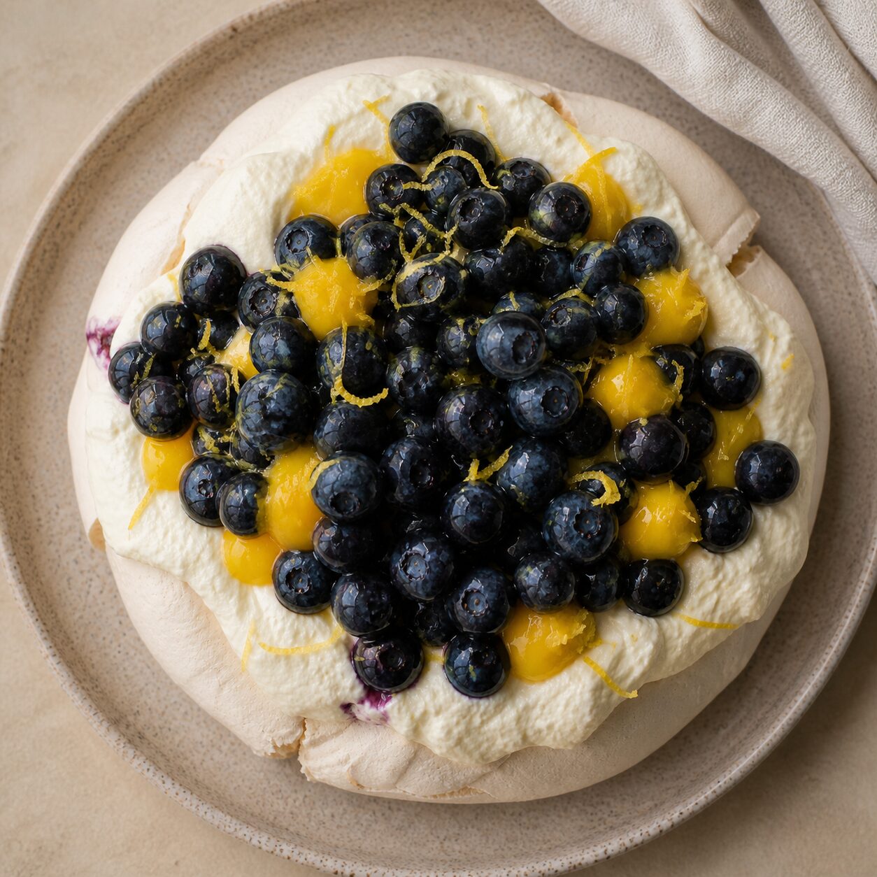 Lemon zest curls over whipped cream on the blueberry pavlova